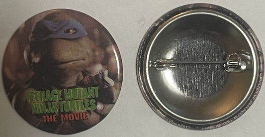 Front and back of circular metal pinback button featuring Donatello from Teenage Mutant Ninja Turtles movie with green text l