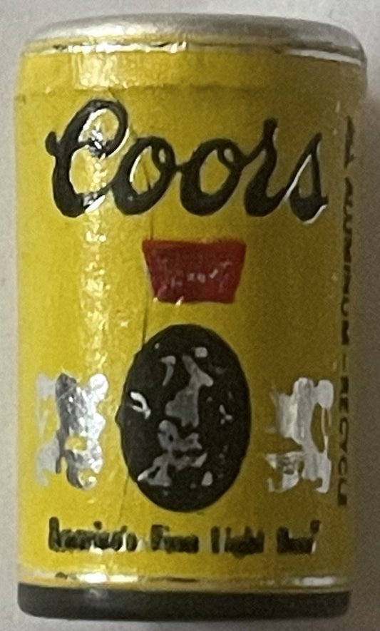 Vintage yellow Coors mini beer can with black script logo and oval portrait medallion, sealed with foil top, viewed at angle