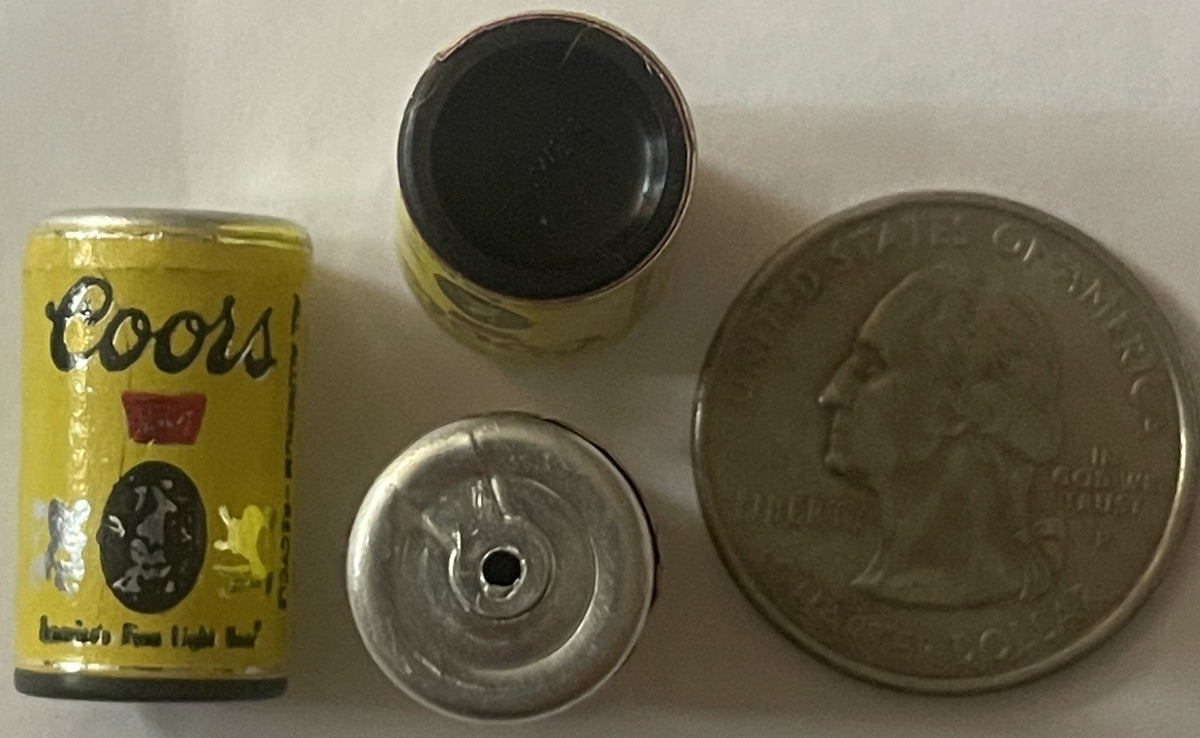Miniature yellow Coors beer can with black and red label displayed next to its metal pull-tab top and a quarter for scale