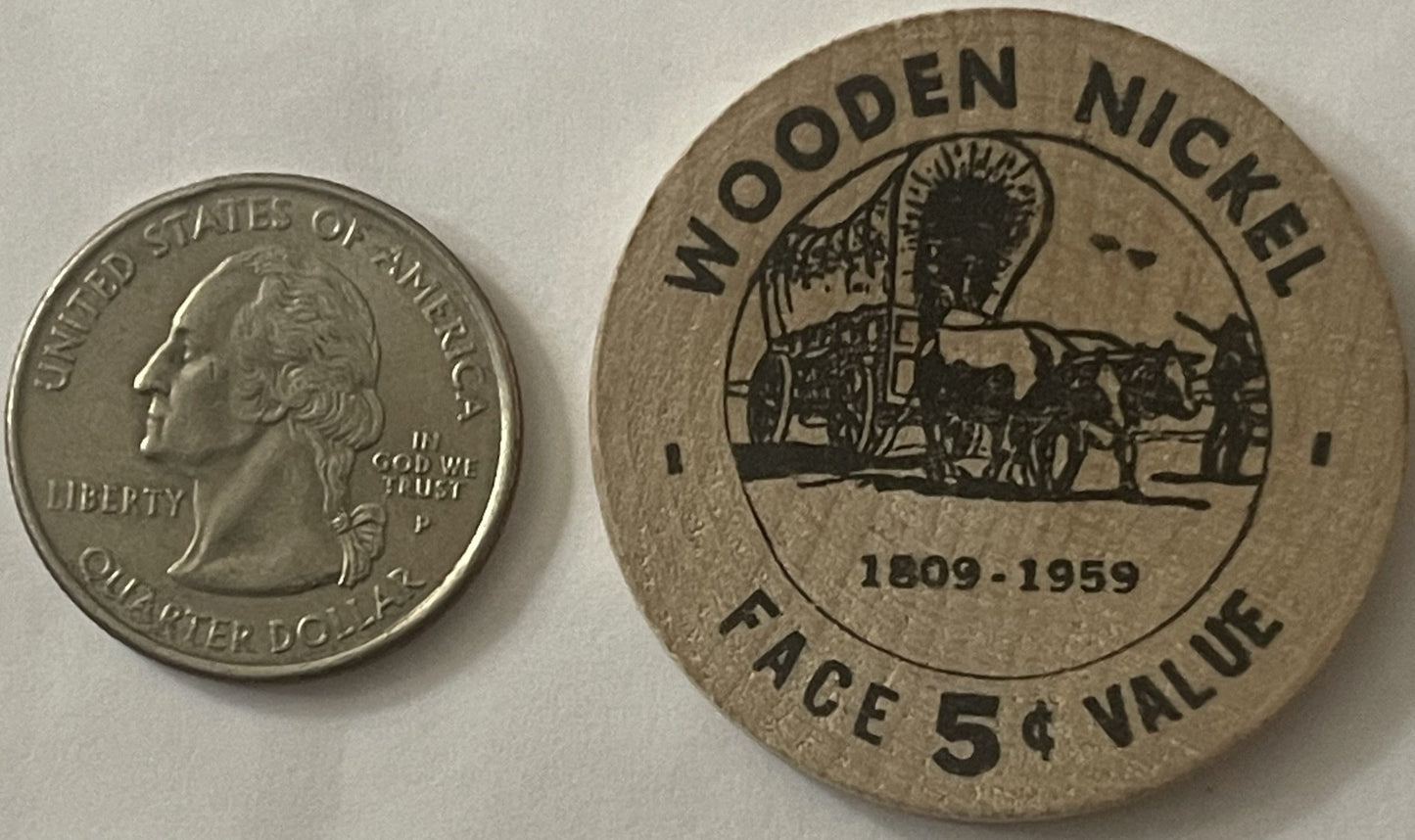 Wooden quarter next to quarter for scale, showing horse-drawn wagon and text "Wooden quarter 1809-1959 Face 5¢ Value