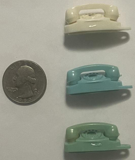 Three miniature ceramic telephone keychains in cream, turquoise, and sage green beside a quarter for scale, shown from above