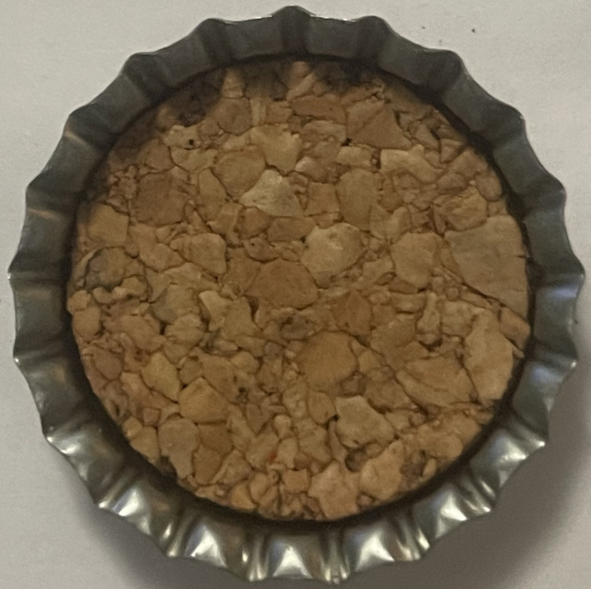 Overhead view of a cork bottle cap with scalloped metal edges, tan cork insert showing cracks and wear, on white background