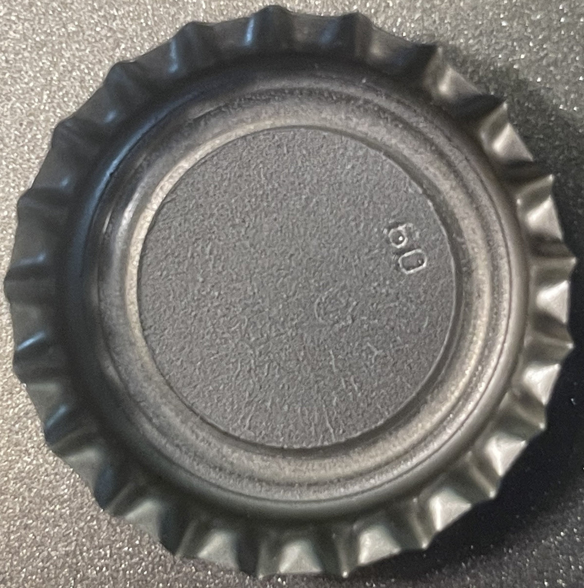Close-up overhead view of a black metal crown bottle cap with ridged edges and embossed number 9 on textured center surface