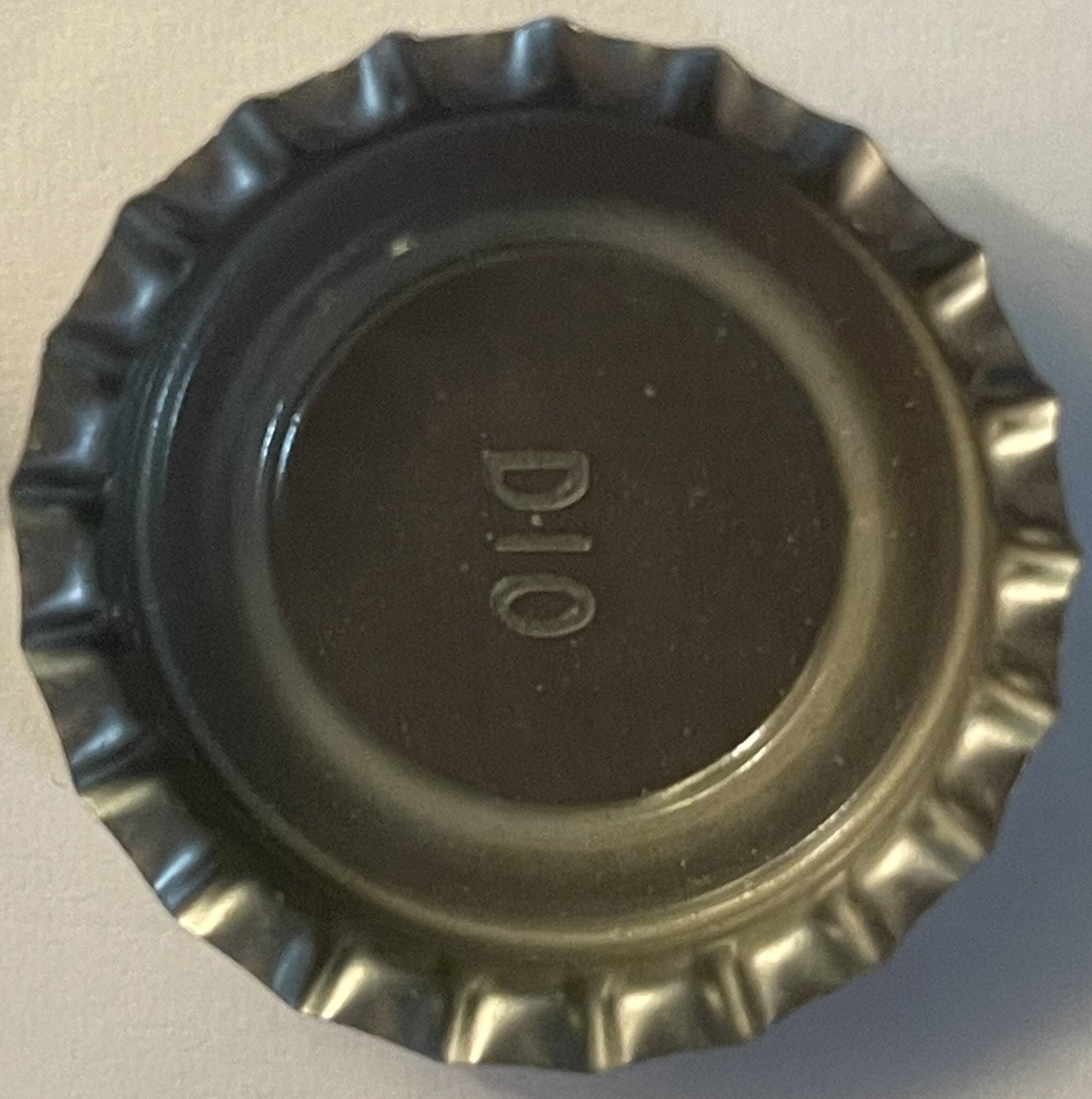 Vintage bottle cap with corrugated metal rim and embossed "YUP" text on dark center, photographed flat against beige surface