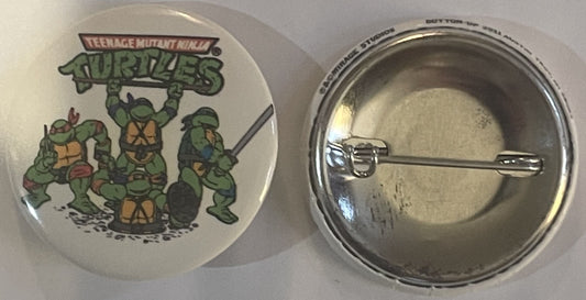 Vintage TMNT pin badge showing four green turtles with "Teenage Mutant Ninja Turtles" text, displayed front and back on white