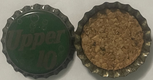 Two views of a metal bottle cap with scalloped edges showing the green interior and cork-lined underside with tan residue
