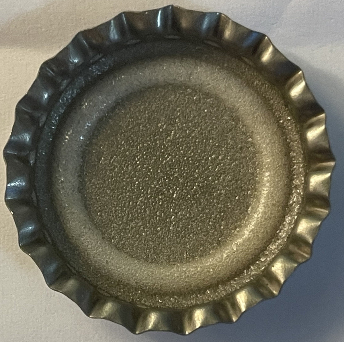 Overhead view of a metal bottle cap with crimped edges and textured surface, showing wear consistent with vintage