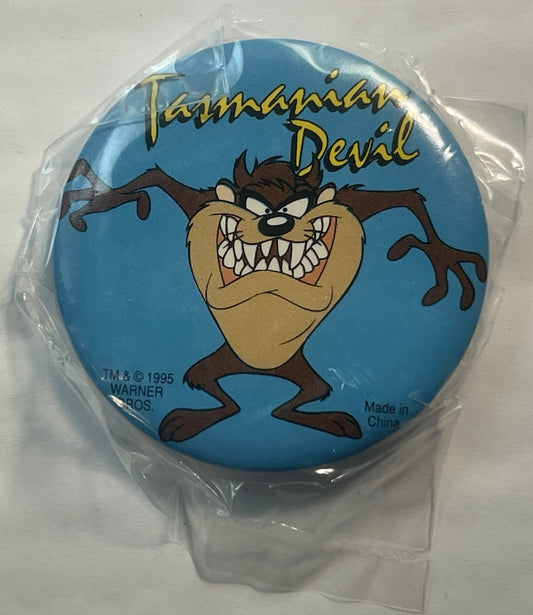 Circular pin featuring angry Tasmanian Devil character with bared teeth on blue background, gold lettering "Tasmanian Devil"