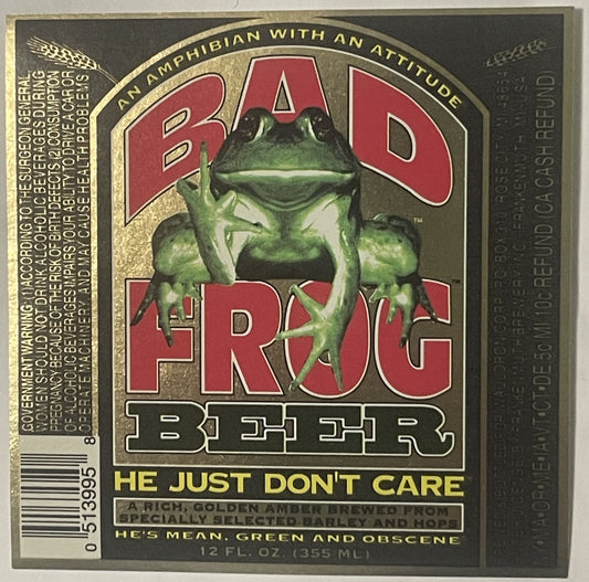 Vintage Bad Frog Beer label featuring a green cartoon frog with raised middle finger, red text, gold borders, and yellow tagline "HE JUST DON'T CARE" on tan and dark background.