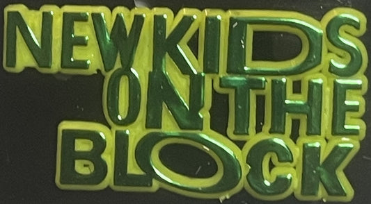 Close-up of yellow and green embossed pin with "New Kids on the Block" text against dark background