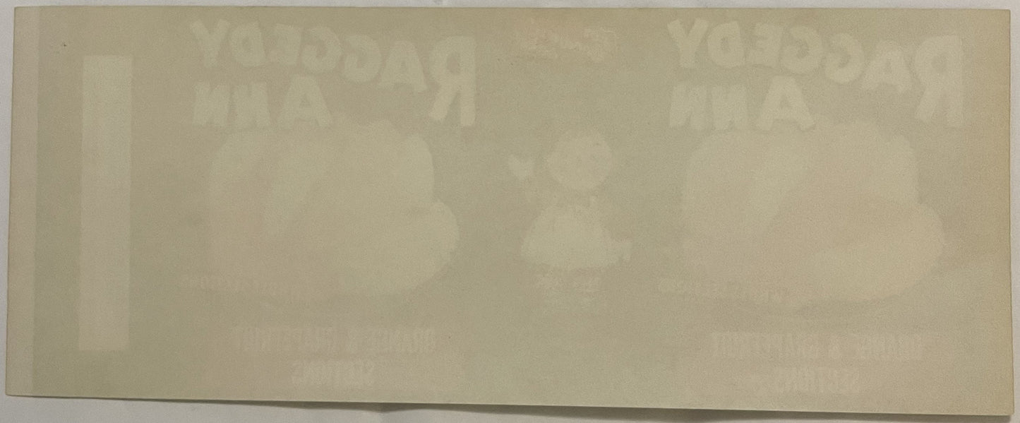 Faded cream-colored vintage can label with barely visible Raggedy Ann imagery and text, photographed flat against white backg