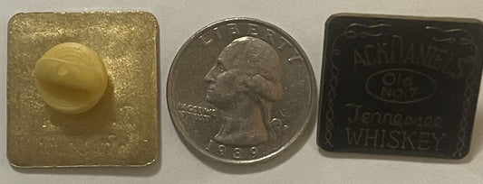 Three vintage items displayed: gold square pin with embossed face, silver quarter coin for scale, and dark rectangular Jack D
