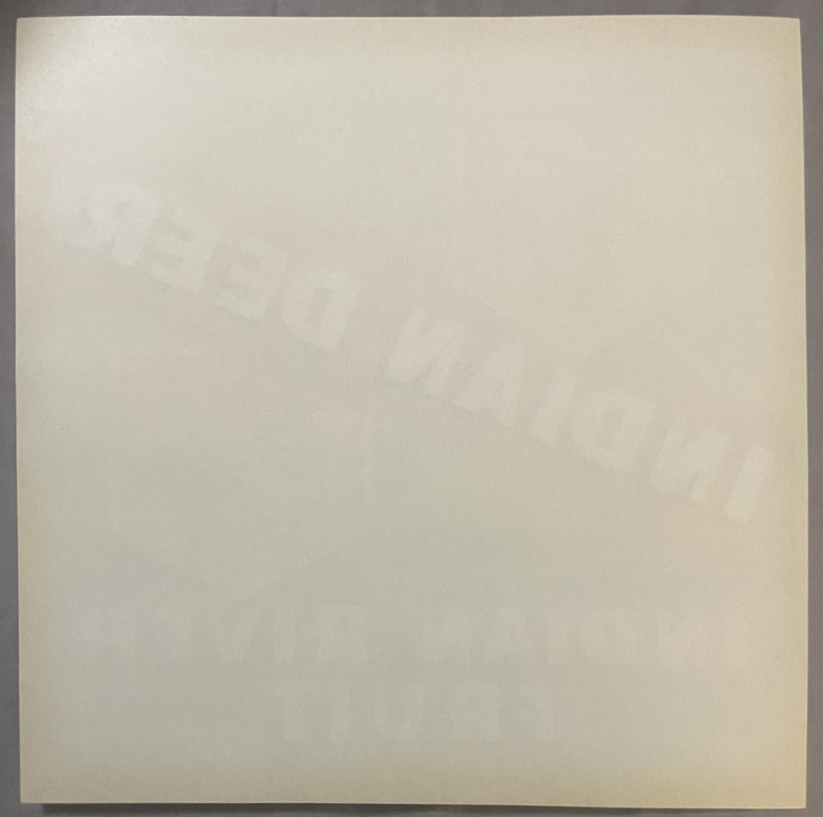 Cream-colored vintage fruit crate label with faint embossed or printed imagery, shown flat against gray surface