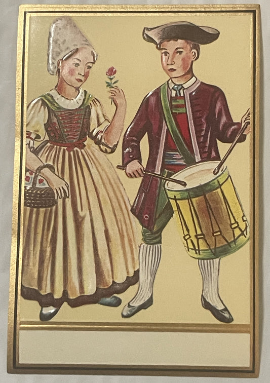 Gold embossed vintage label showing a girl in white dress holding a flower and a boy drummer in maroon coat and yellow breech