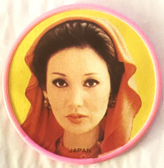 Circular pocket mirror with pink rim featuring portrait of Asian woman in red garment against yellow background, "JAPAN" prin
