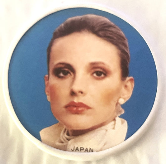 Circular pocket mirror with blue background portrait of a woman with dark hair and light skin wearing a beige turtleneck, lab