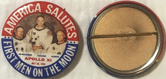 Vintage Apollo XI pin showing three astronauts in spacesuits with "America Salutes First Men on the Moon" text, displayed fro