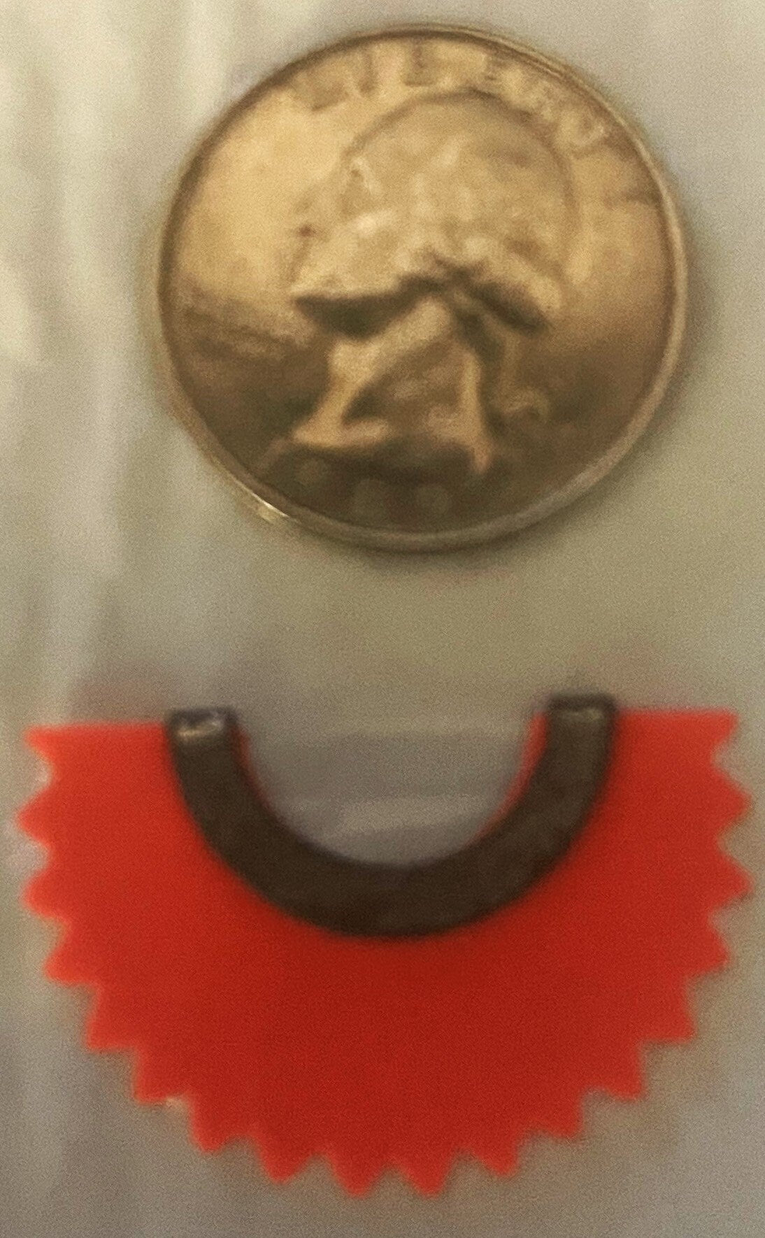 Circular brass bird call with embossed design shown above red decorative backing material