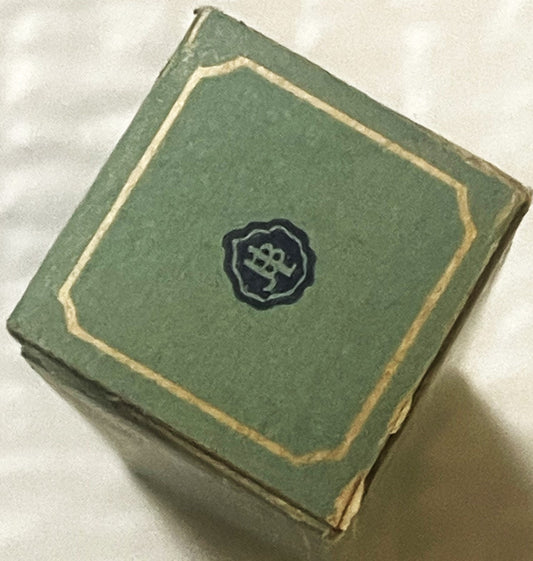 Green cloth-covered antique box with gold trim and dark emblem on front, angled view on white background