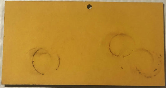 Faded yellow advertising card with two faint circular marks and a hole punched at top center