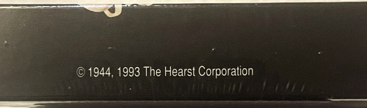 Close-up of sealed box bottom showing copyright text "© 1944, 1993 The Hearst Corporation" on dark background with tape at to