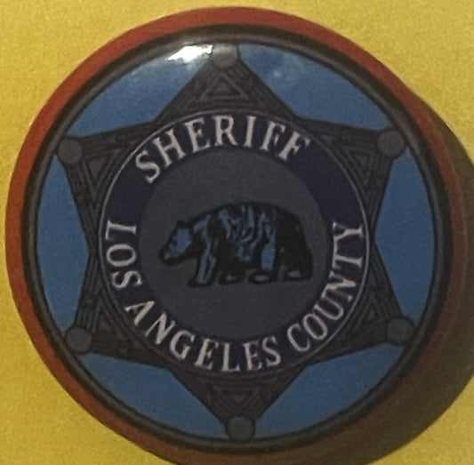 Circular tin litho badge with blue and black star design reading "Los Angeles County Sheriff" with bear emblem, mounted on ye