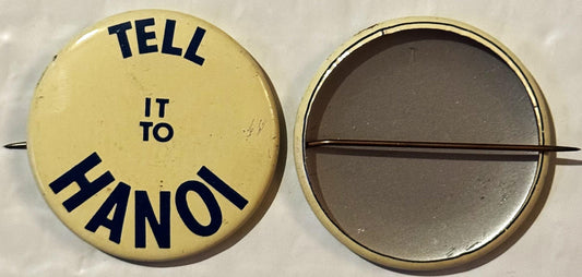 Front and back views of a cream-colored round pinback button with navy text reading "TELL IT TO HANOI" arranged in a circle.