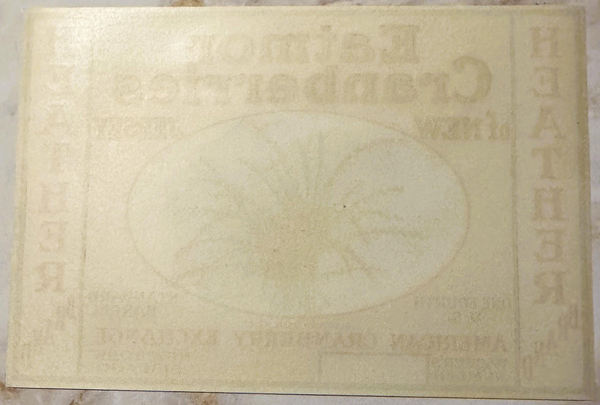Cream-colored vintage cranberry barrel label with faded embossed text and decorative border, photographed flat against light