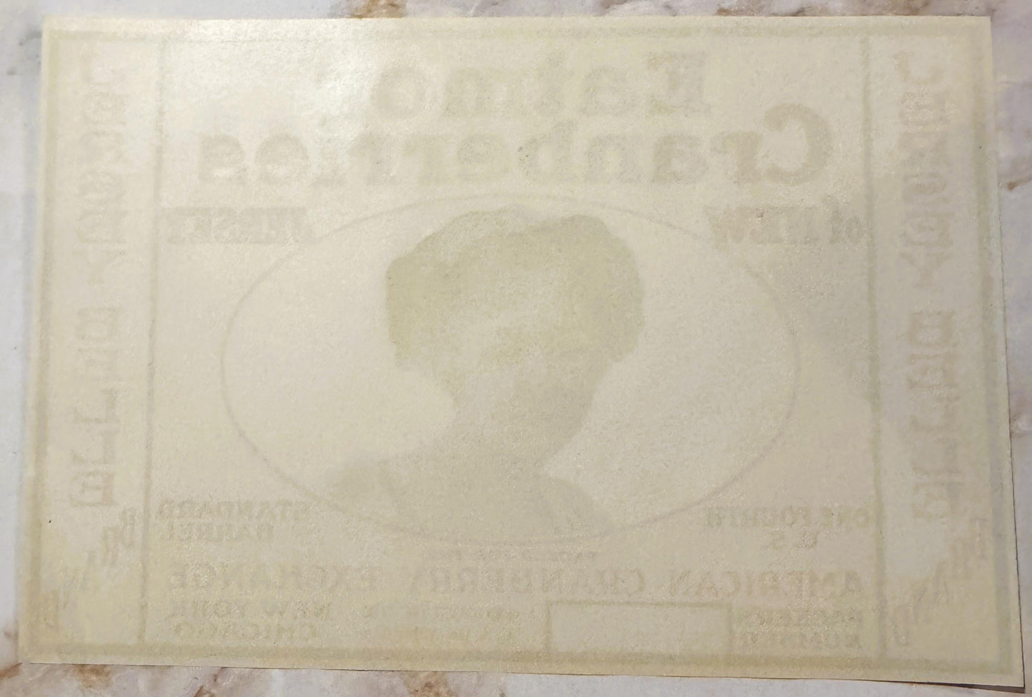 Cream-colored vintage cranberry barrel label with faded embossed design showing a profile portrait in center, text visible ar