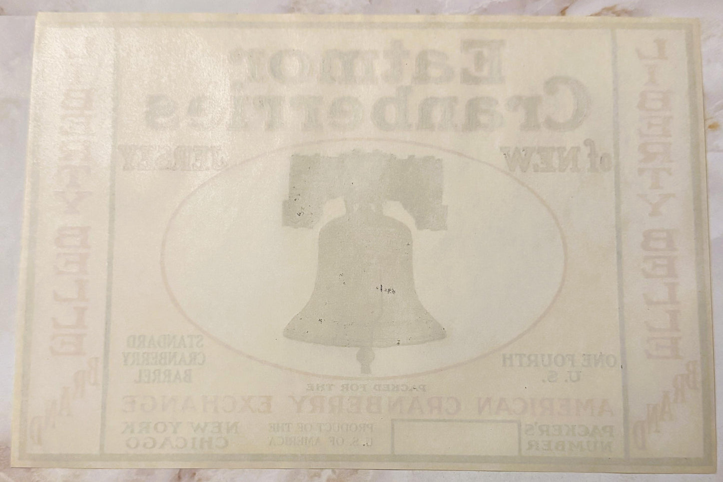Faded cream-colored vintage cranberry barrel label featuring embossed Liberty Bell in oval frame, text largely illegible due