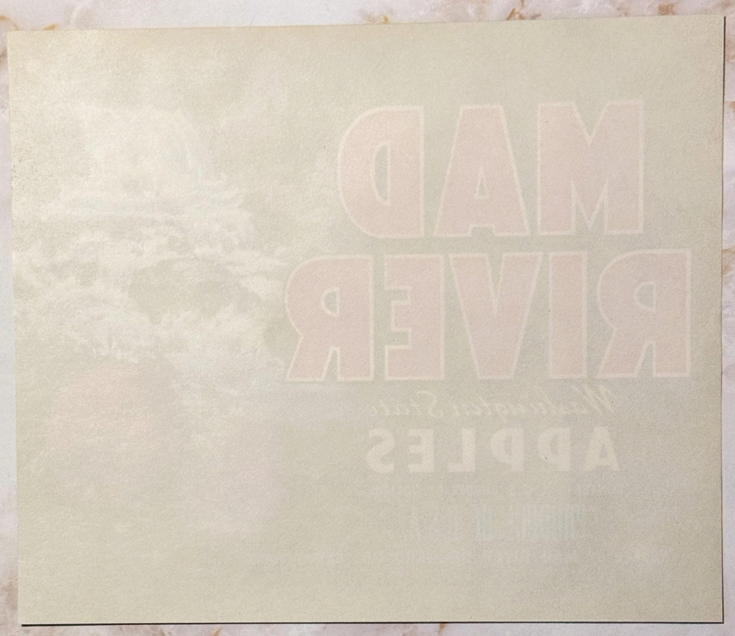 Cream-colored vintage apple crate label with embossed text reading "MAD RIVER" and additional text below, photographed flat a