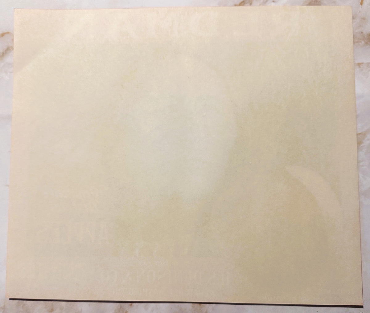 Blank cream-colored vintage apple crate label on marble surface with dark line at bottom edge