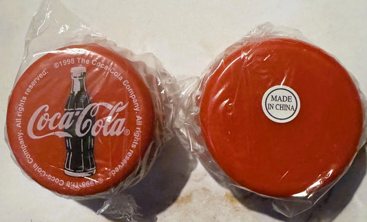 Two red Coca-Cola yo-yos in plastic packaging, left showing 1998 branding with bottle, right labeled "Made in China