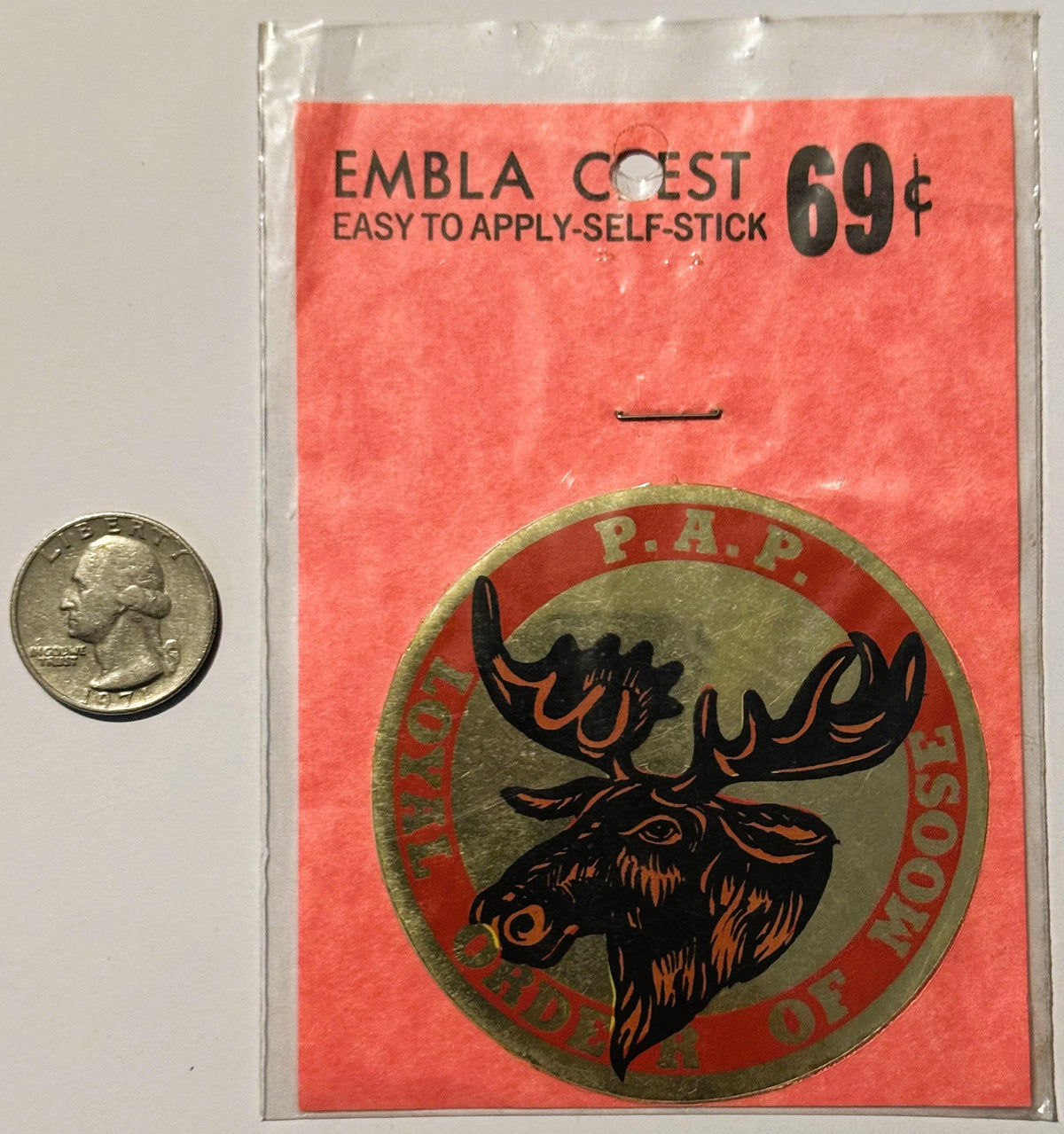 Vintage self-stick emblem decal priced at 69 cents, featuring a moose head in brown and orange on tan circle, next to quarter
