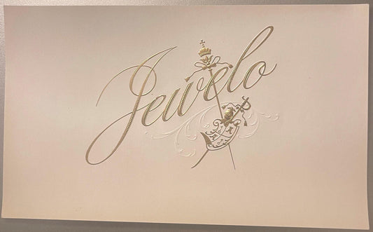 Gold embossed cigar label on cream cardstock reading "Jewelo" in flowing script with decorative coat of arms and ornamental f