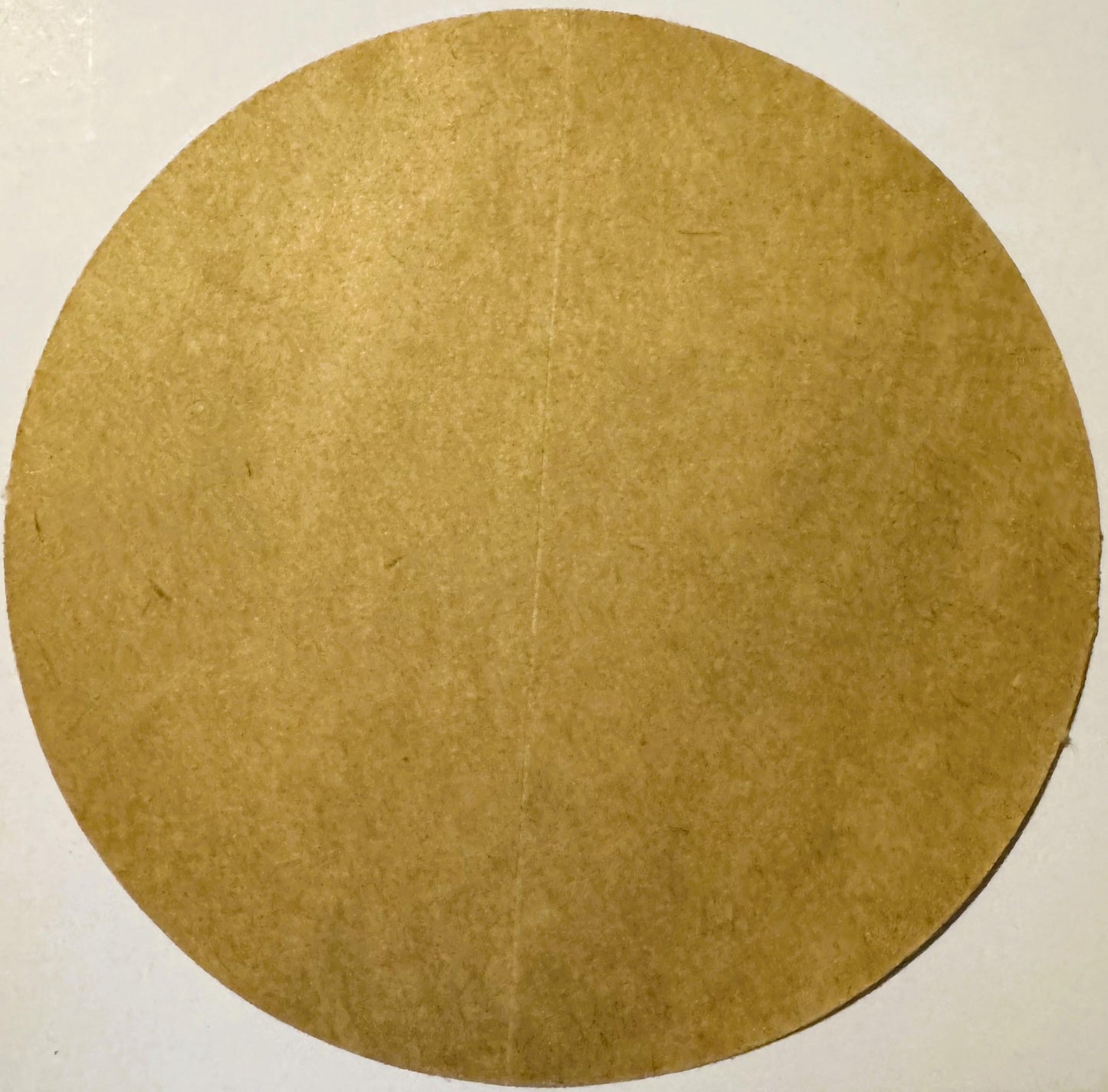 Circular tan cardboard backing or substrate with textured surface, photographed straight-on against white background
