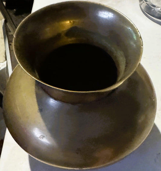 Overhead view of a round brass vessel with a flared rim and dark patina, photographed on a white surface