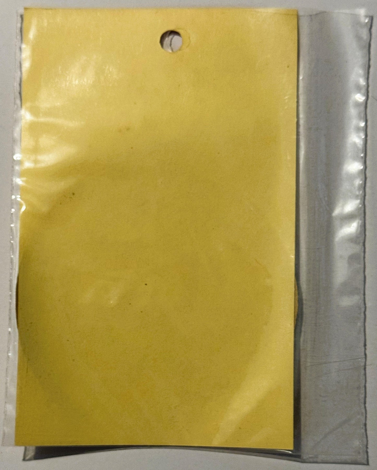 Bright yellow rectangular decal in clear plastic packaging with small hole for hanging, shown against white background