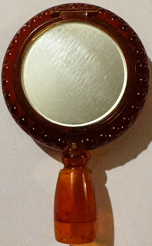 Vintage red plastic hand mirror with ornate molded frame and pale green circular mirror surface, wooden handle, photographed