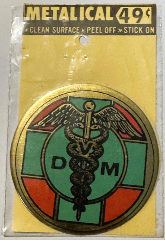 Metallic gold vintage decal sticker with caduceus medical symbol and "D M" letters on green and red quarters, packaged on yel