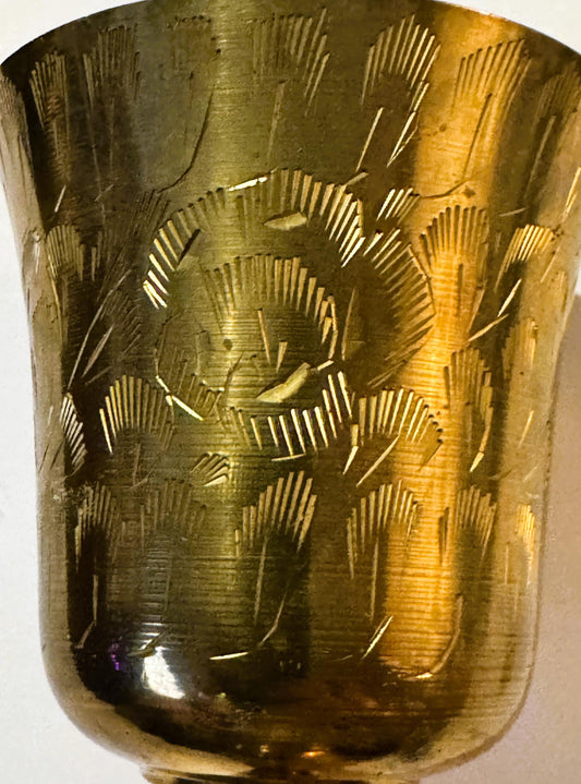 Vintage brass goblet with bright-cut etched floral and geometric patterns, shown against plain background at close angle