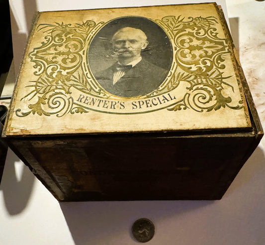 Ornate gold-embossed cigar box lid with portrait medallion labeled "Renter's Special," displayed with coin for scale