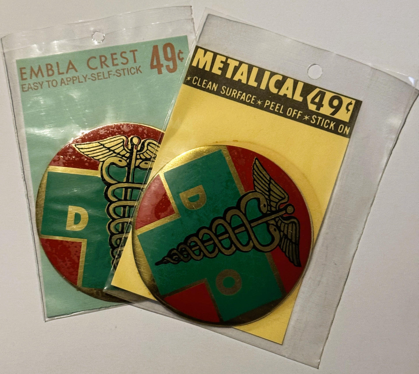 Two unopened vintage decal packages featuring a medical caduceus symbol in red, green, and gold, priced at 49¢ each