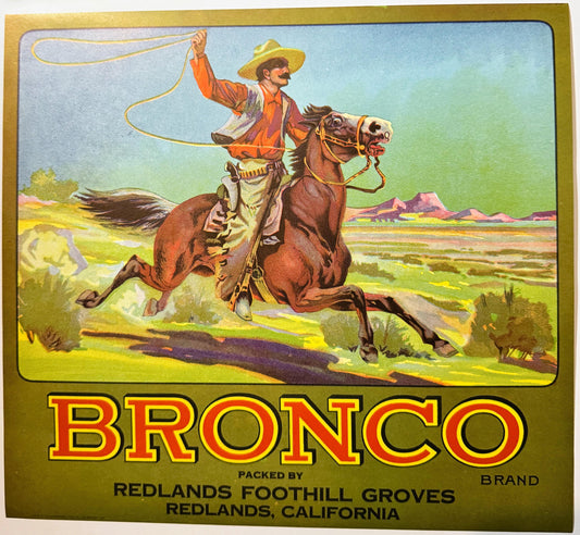 Vintage fruit crate label featuring a cowboy on horseback with lasso against desert landscape, "Bronco Brand" text, packed by