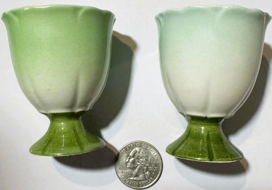 Two green and white ceramic egg cups with pedestal bases shown with a quarter for scale