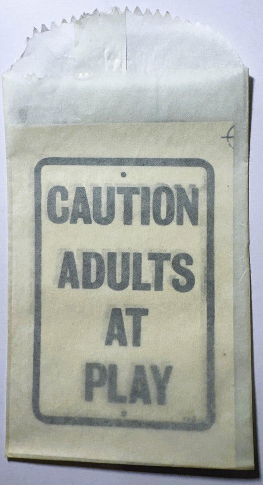 Vintage paper packet with "CAUTION ADULTS AT PLAY" printed text, shown against white background with crinkled top edge