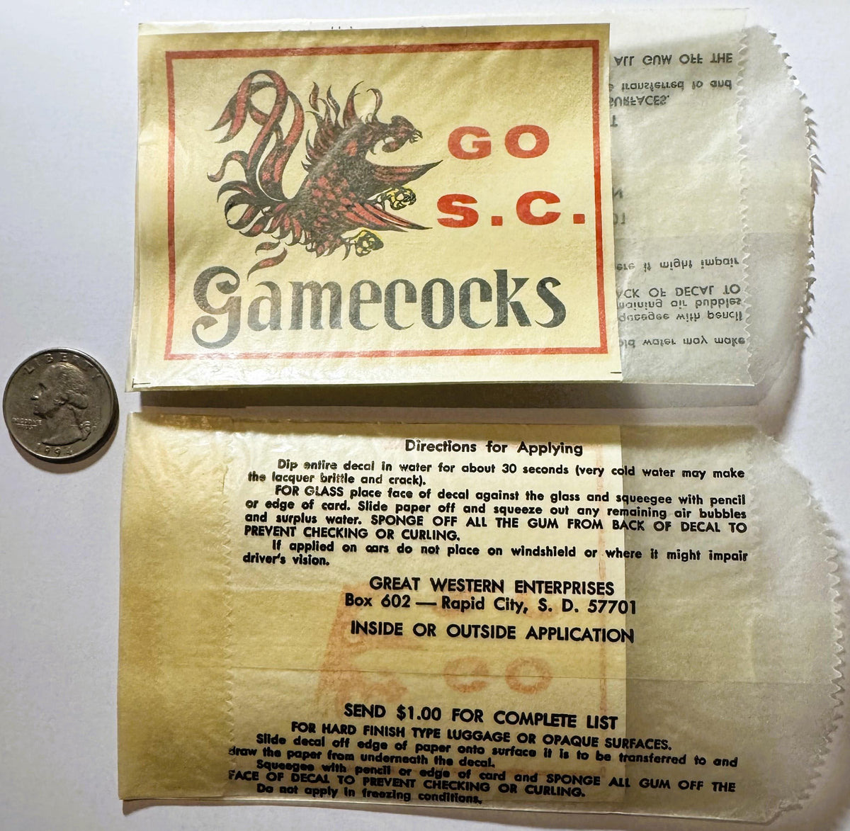 Vintage South Carolina Gamecocks water-transfer decal in original packaging with quarter for scale, showing red gamecock logo