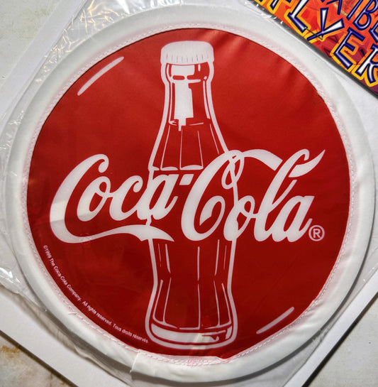 White plastic disc with red circular center featuring Coca-Cola script logo, bottle silhouette, and registered trademark symb