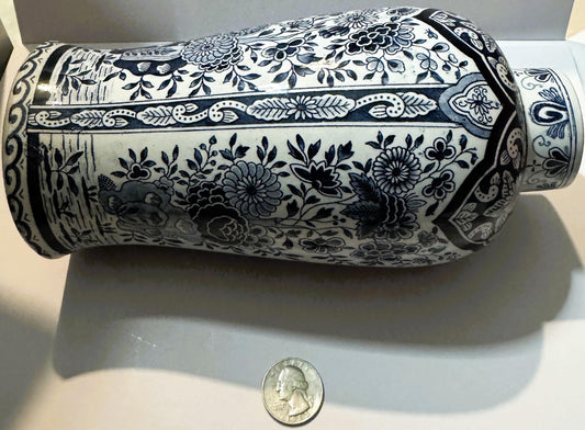 Cylindrical blue and white ceramic vase with floral patterns, shown horizontally next to a quarter for scale