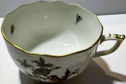 Cream porcelain teacup with gold rim, hand-painted birds and insects inside and on exterior, viewed from above at an angle sh